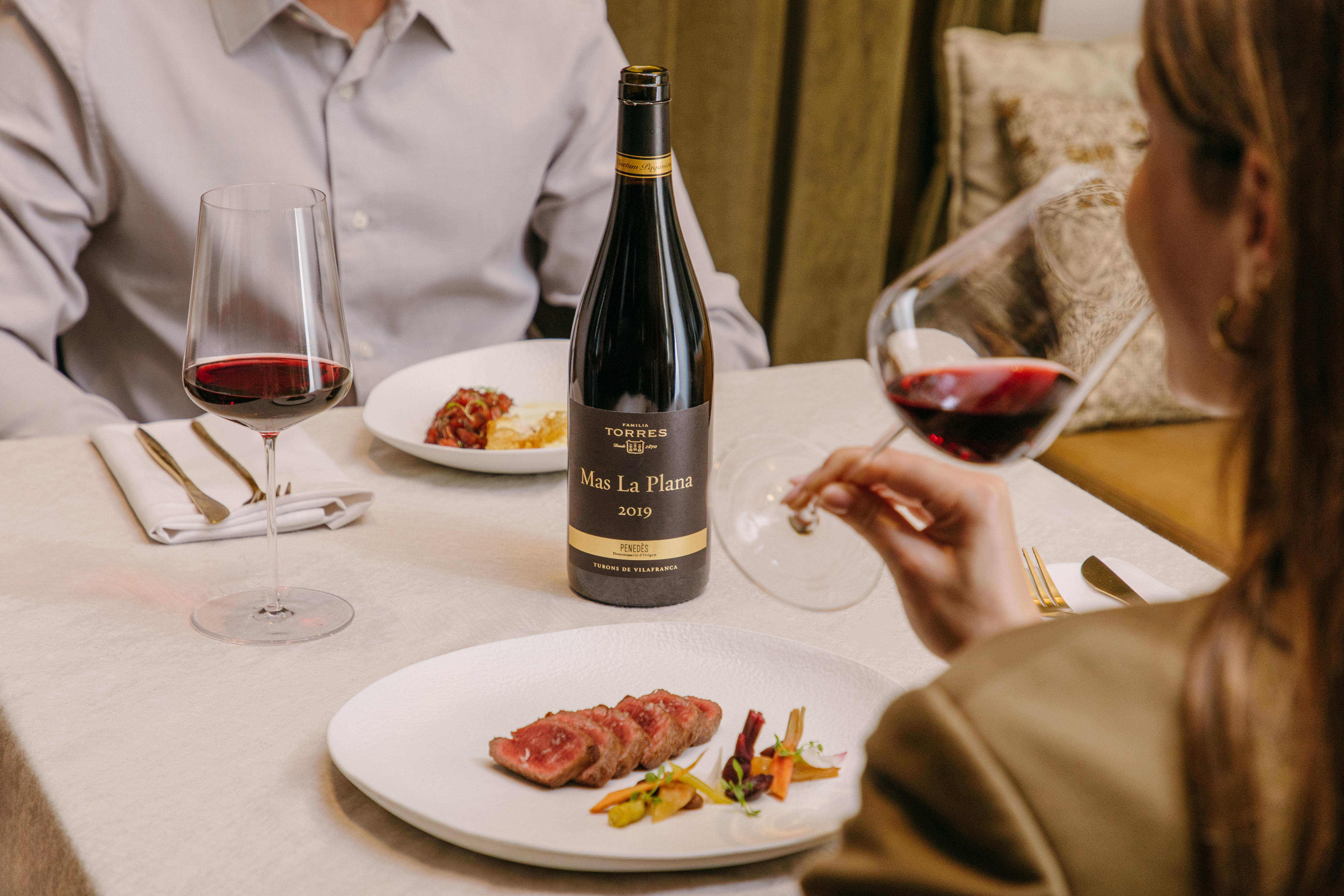 Pareja disfrutando de una comida alrededor del vino Mas La Plana, propiedad de Familia Torres. 