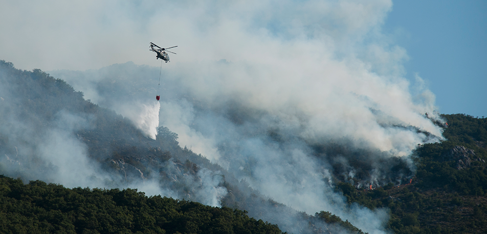 Megaincendios, causa y efecto del cambio climático Un helicóptero realizando tareas de exterminación de un incendio en un entorno montañoso